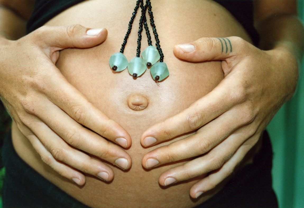 A pregnant person cradling their belly with hands adorned with jewelry, showcasing a moment of maternal and metaphysical connection.