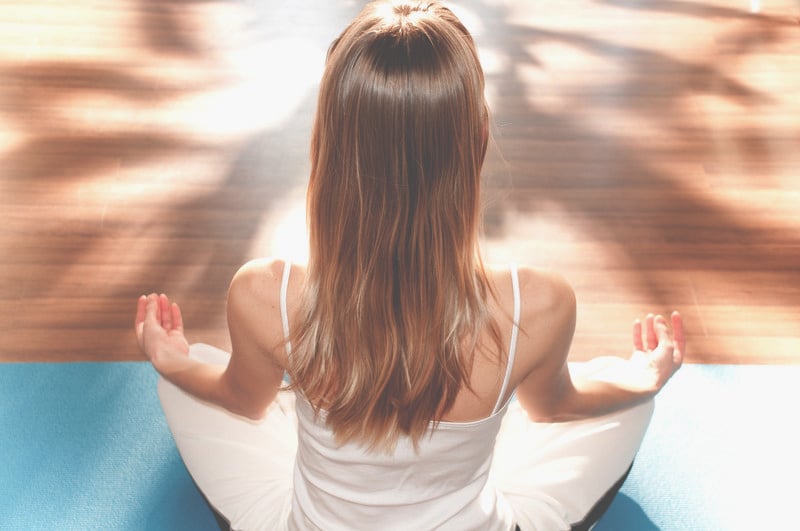 A serene moment of meditation: woman practicing mindfulness with a yoga pose in a room bathed with warm sunlight and surrounded by new age products.