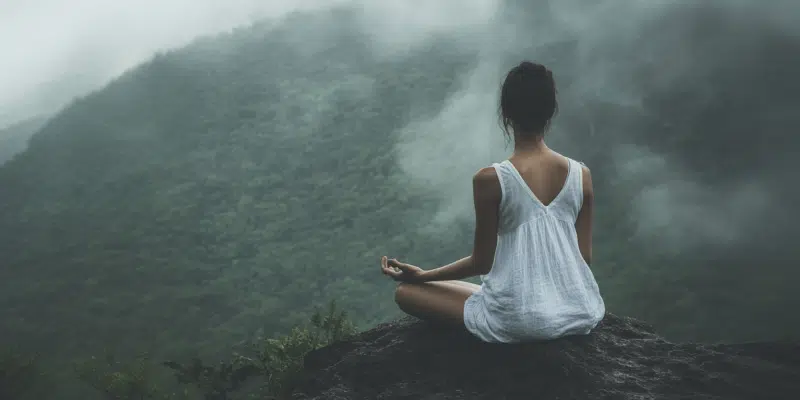 A woman practicing mindful breathing while meditating on a misty mountaintop, embracing serenity and nature.