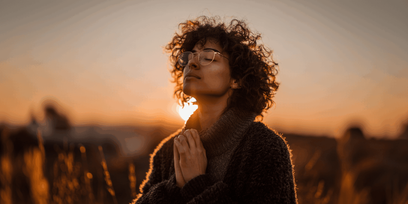 a woman with curly hair and glasses praying outside