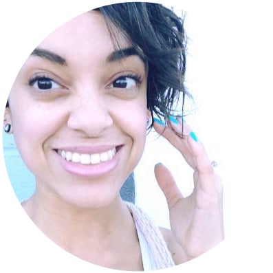 final-moonie A joyful woman with a bright smile, tousled hair, and teal painted nails posing for a lighthearted selfie in front of her favorite metaphysical shop.