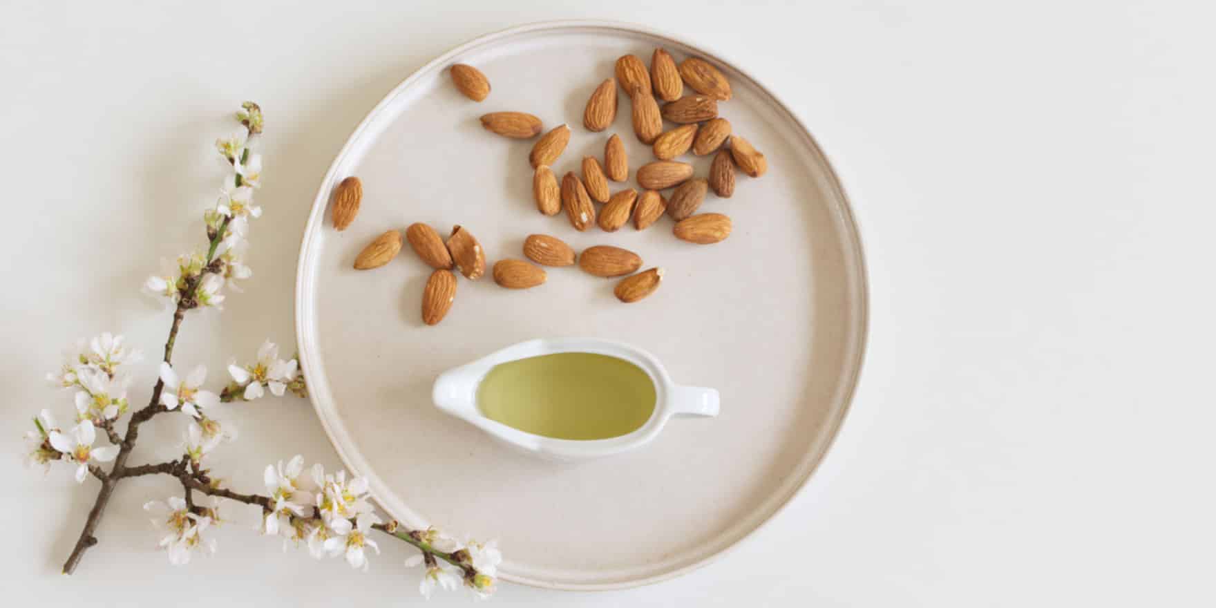 almonds on a round white plate with oil and an almond flower branch next to it