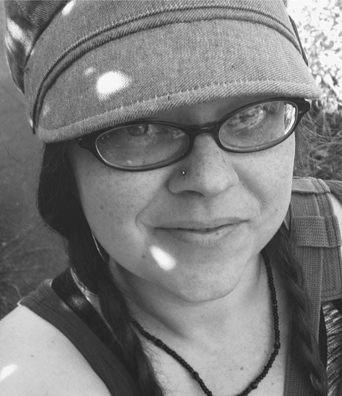 A monochrome close-up of a smiling person wearing glasses, a nose piercing, and a witchy beanie hat with a braided hairstyle, outdoors on a sunny day.
