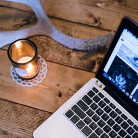 Free Materia Magicka Worksheets 4 A cozy workspace featuring an open laptop, a lit candle on a decorative holder with witchy vibes, and a rustic wooden table set against a warm, homey backdrop.