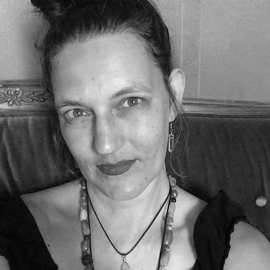 Black and white portrait of a woman with an updo hairstyle, witchy earrings, wearing a necklace, and giving a subtle smile to the camera.