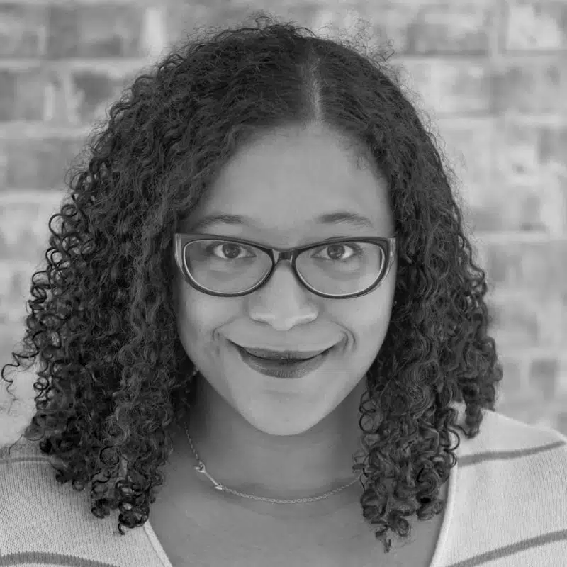 Black and white portrait of a smiling woman with curly hair and glasses in a metaphysical shop.