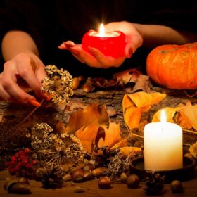 Samhain Ritual: Connect to your Spirit Family for Growth 51 A person arranges witchy elements like dried flowers, leaves, and acorns on a wooden surface, illuminated by the warm glow of candles, with a small pumpkin adding to the seasonal atmosphere.
