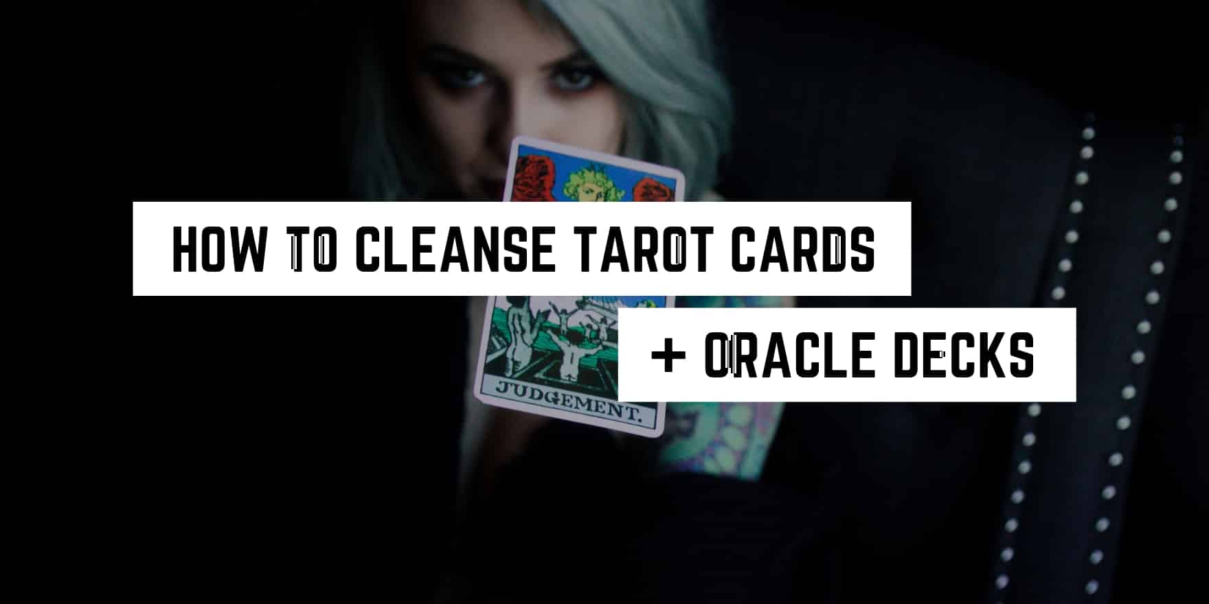 A mysterious figure holding tarot cards with text overlay 'how to cleanse tarot cards + oracle decks in a witchy manner'.