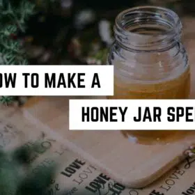 A spiritual jar of honey placed on a wooden board next to some greenery with text overlay "how to make a honey jar spell".