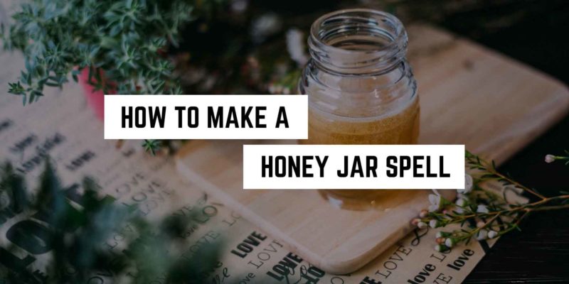 A spiritual jar of honey placed on a wooden board next to some greenery with text overlay "how to make a honey jar spell".