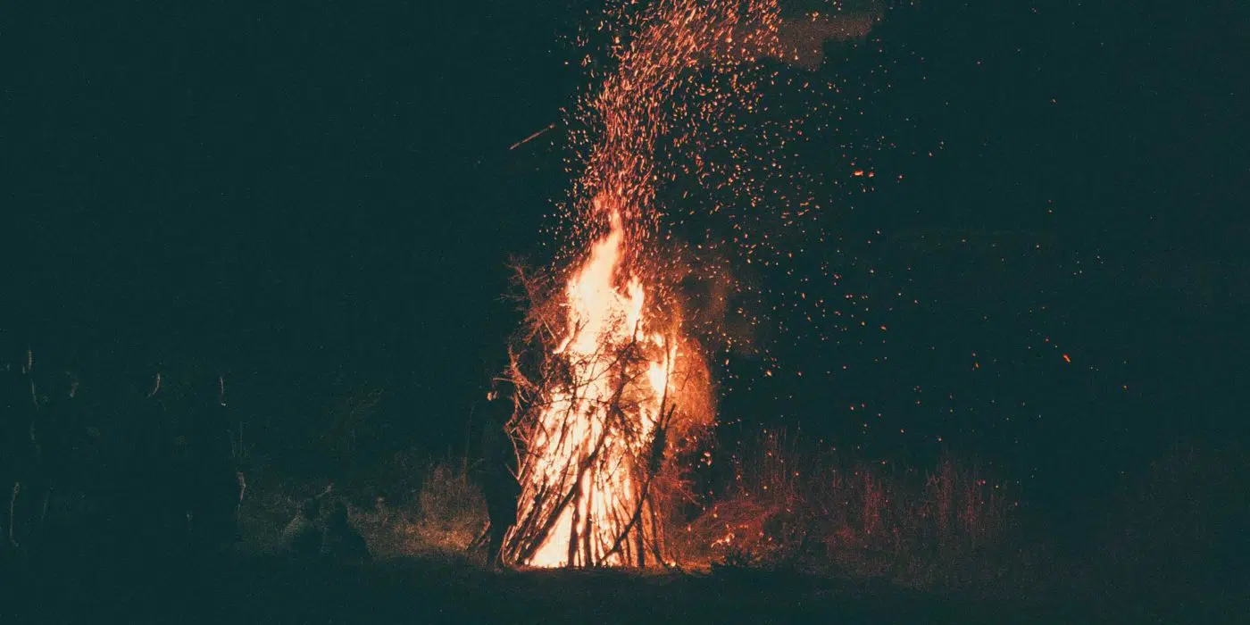 Midsummer: The Reawakening of a Witch 1 A bonfire crackling in the night, casting a warm, witchy glow as sparks dance into the dark sky.