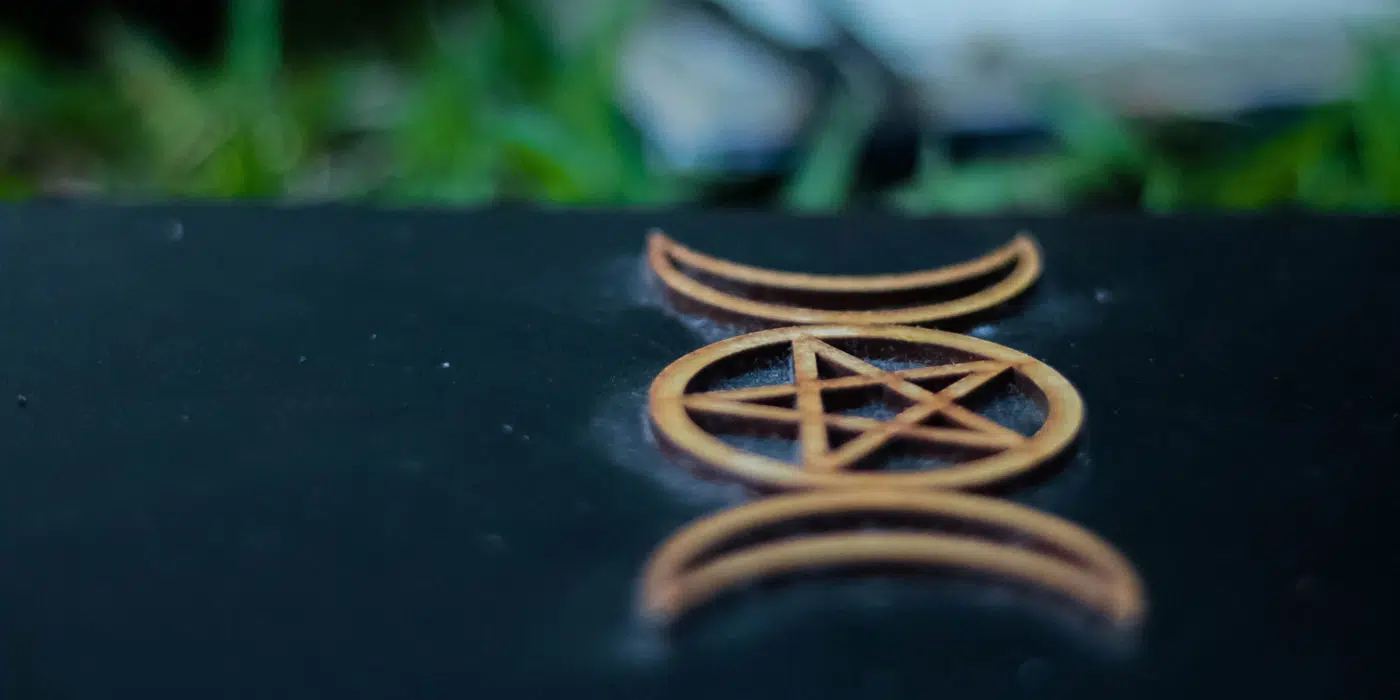 Close-up of a golden pentacle symbol, with occult vibes, etched on a dark surface, with soft-focus greenery in the background.