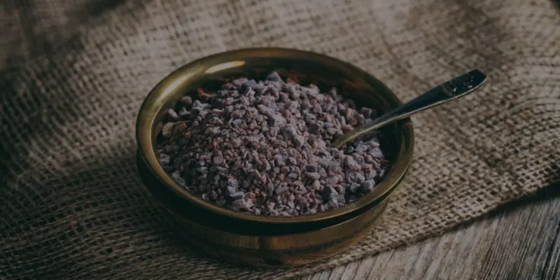 A rustic bowl filled with coarse sea salt accompanies a spoon, set against a textured burlap background, perfect for any witchy or new age product ritual.