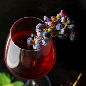 Mabon Ritual for Ultimate Balance 42 A glass of red wine elegantly accompanied by a cluster of grapes against a dark, witchy background.