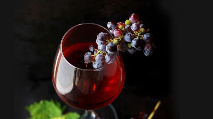 Mabon Ritual for Ultimate Balance 9 A glass of red wine elegantly accompanied by a cluster of grapes against a dark, witchy background.