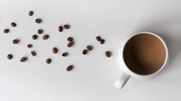 Magical Properties of Coffee | Materia Magicka 7 A cup of coffee with scattered whole beans on a white surface, suggesting a fresh and aromatic start to the day, evoking a spiritual awakening.