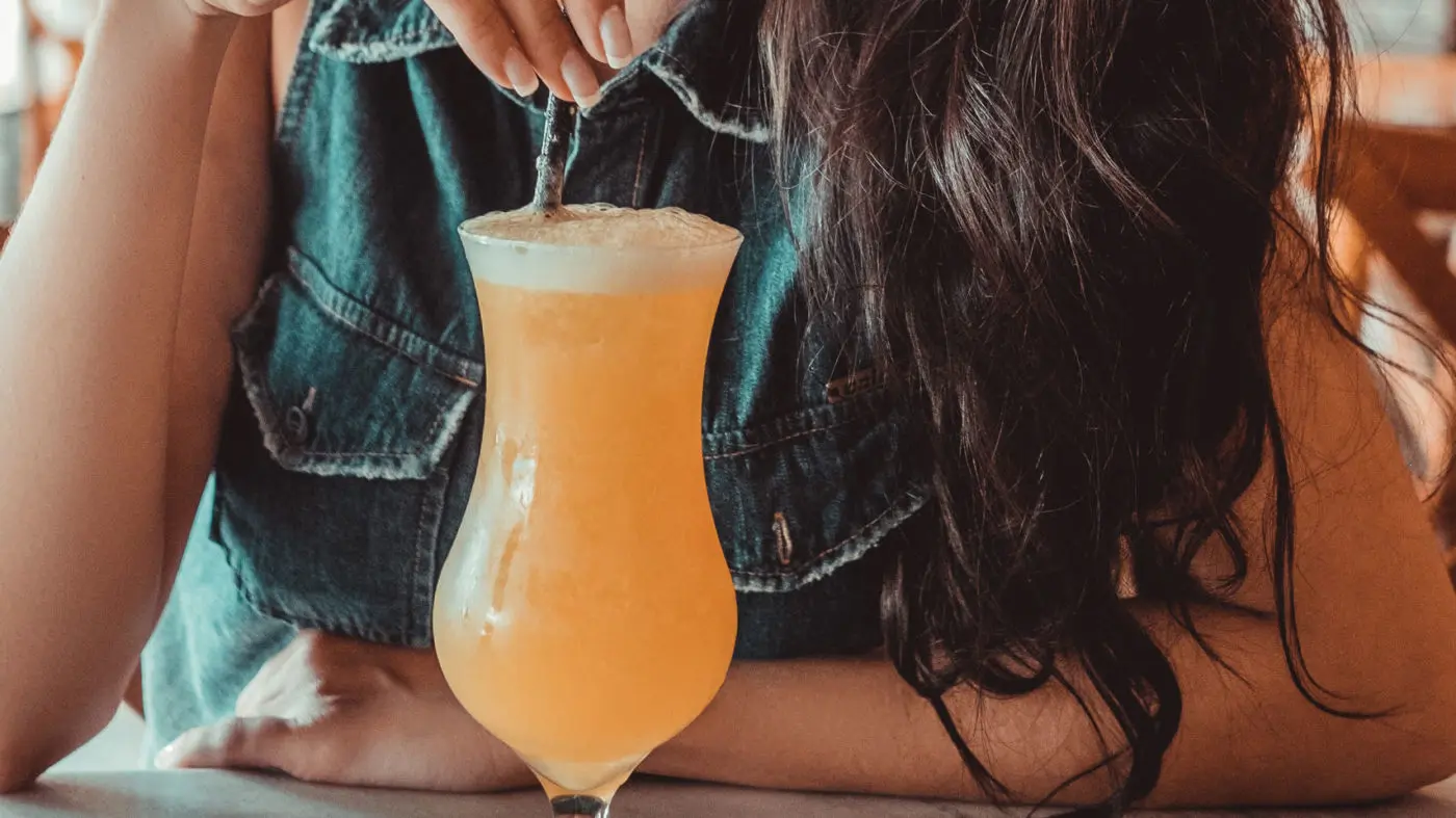 Pumpkin Juice Recipe 1 A person enjoying a refreshing orange slush drink in a tall glass at a cozy cafe turned metaphysical shop.