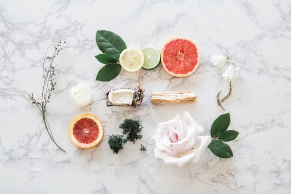 5 Ways to Use Florida Water Cologne 8 Flat lay arrangement of botanical and spiritual elements including citrus slices, herbs, and flowers on a marble surface.