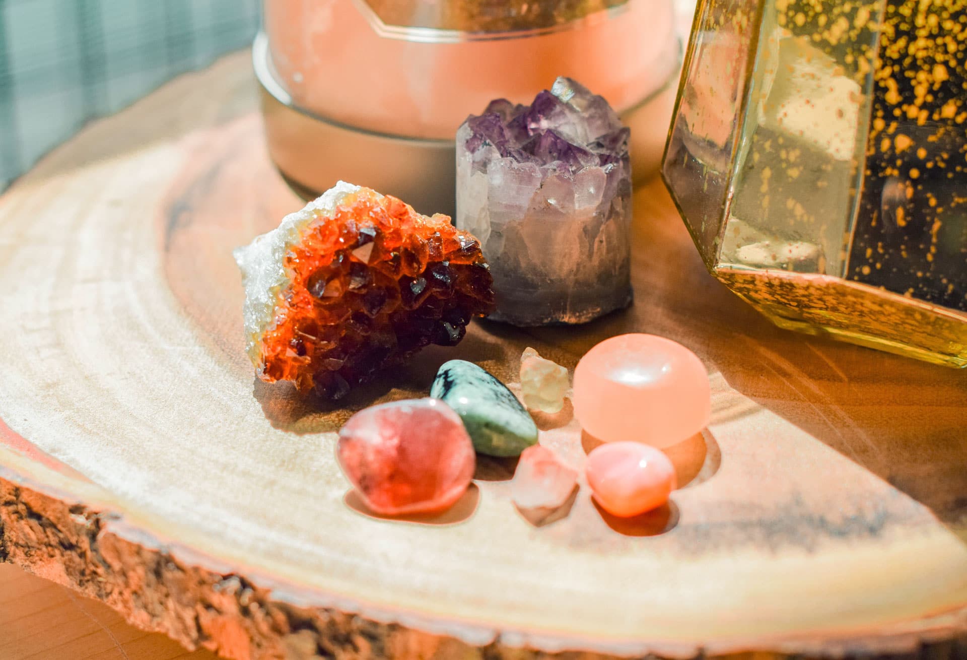 A warm-hued still life photo featuring a collection of vibrant crystals and gemstones artfully arranged on a wooden surface, embodying a witchy vibe with a softly blurred background suggesting a cozy interior setting