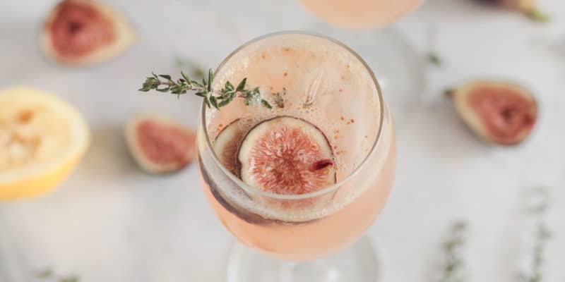 Magical Properties of Thyme | Thyme Materia Magicka 9 A refreshing fig cocktail garnished with a sprig of thyme and a slice of fig, with a subtle backdrop of fig halves and metaphysical herbs.