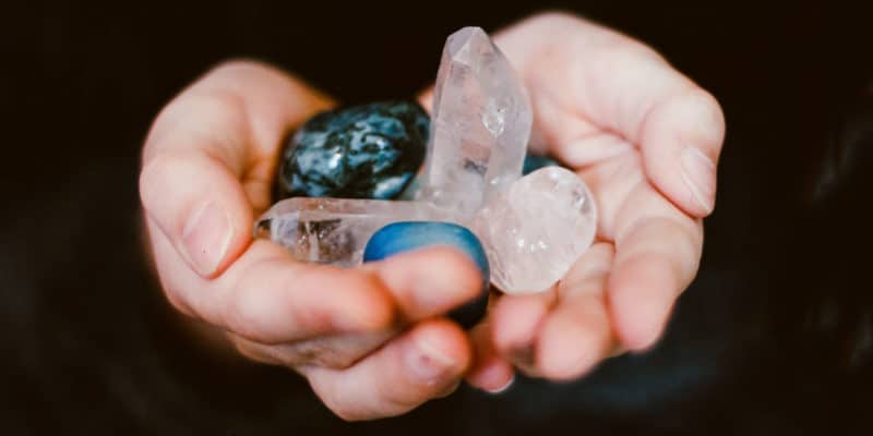 The 7 Best Crystals for Mercury Retrograde 8 A close-up of a person's cupped hands gently holding a collection of various translucent and colored gemstones, radiating a witchy, metaphysical aura.