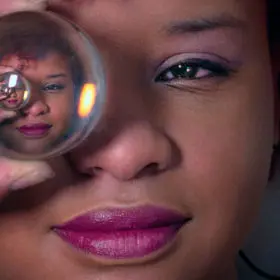 Close-up of a woman holding a crystal ball near her eye, with the reflection in the ball creating an intriguing perspective, perfect for any metaphysical shop's new age product showcase.