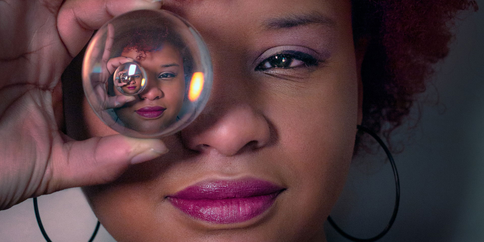 Close-up of a woman holding a crystal ball near her eye, with the reflection in the ball creating an intriguing perspective, perfect for any metaphysical shop's new age product showcase.