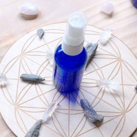 A bottle of essential oil spray on a wooden table with a geometric pattern, surrounded by an array of crystal stones, evoking a sense of tranquility and metaphysical wellness.