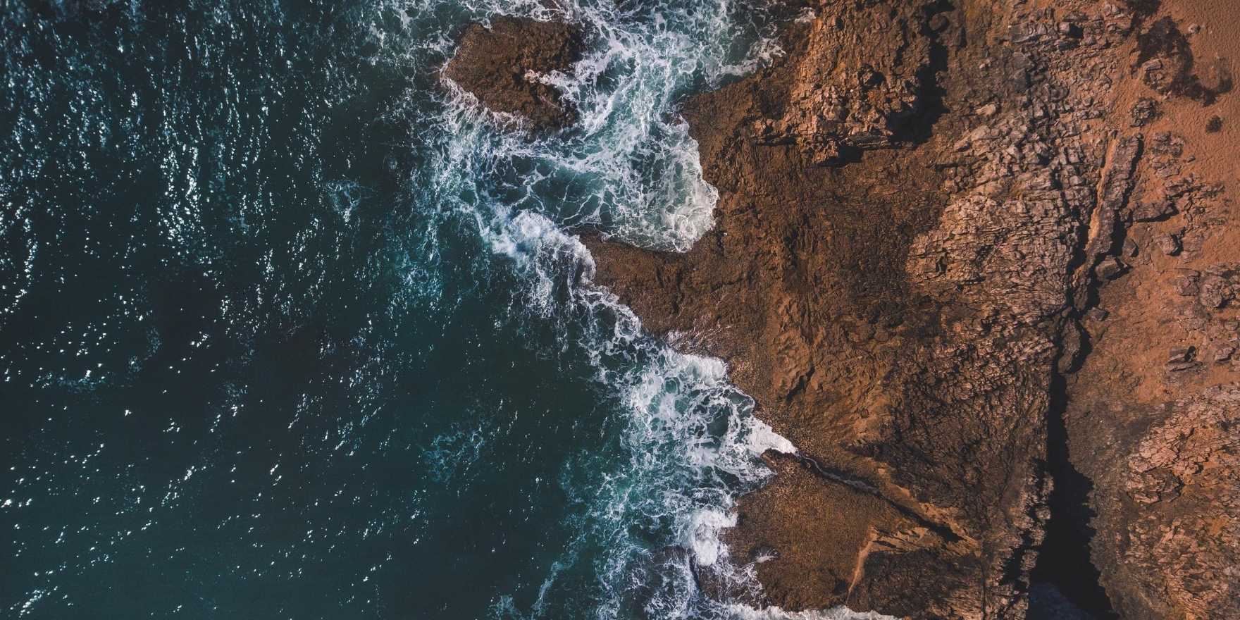 Aerial view of rocky coastline with metaphysical waves crashing against the shore.