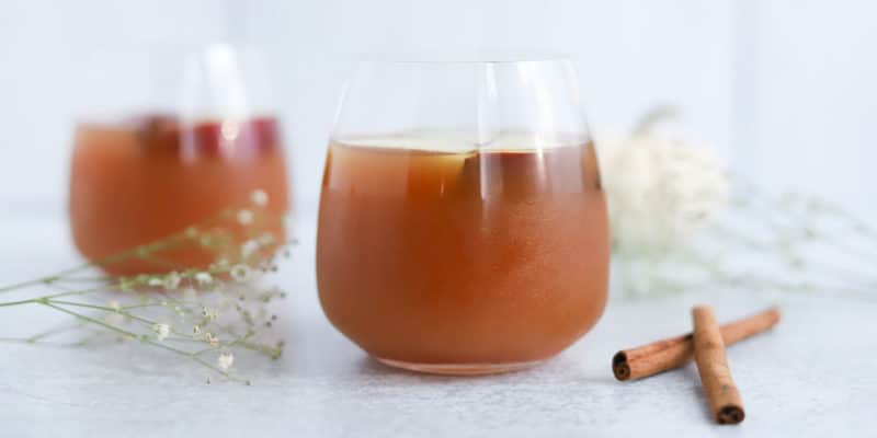Instant Pot Apple Cider Recipe 9 Two glasses of iced tea with a hint of cinnamon, accompanied by delicate white flowers, offering a refreshing moment on a serene backdrop infused with metaphysical energy.