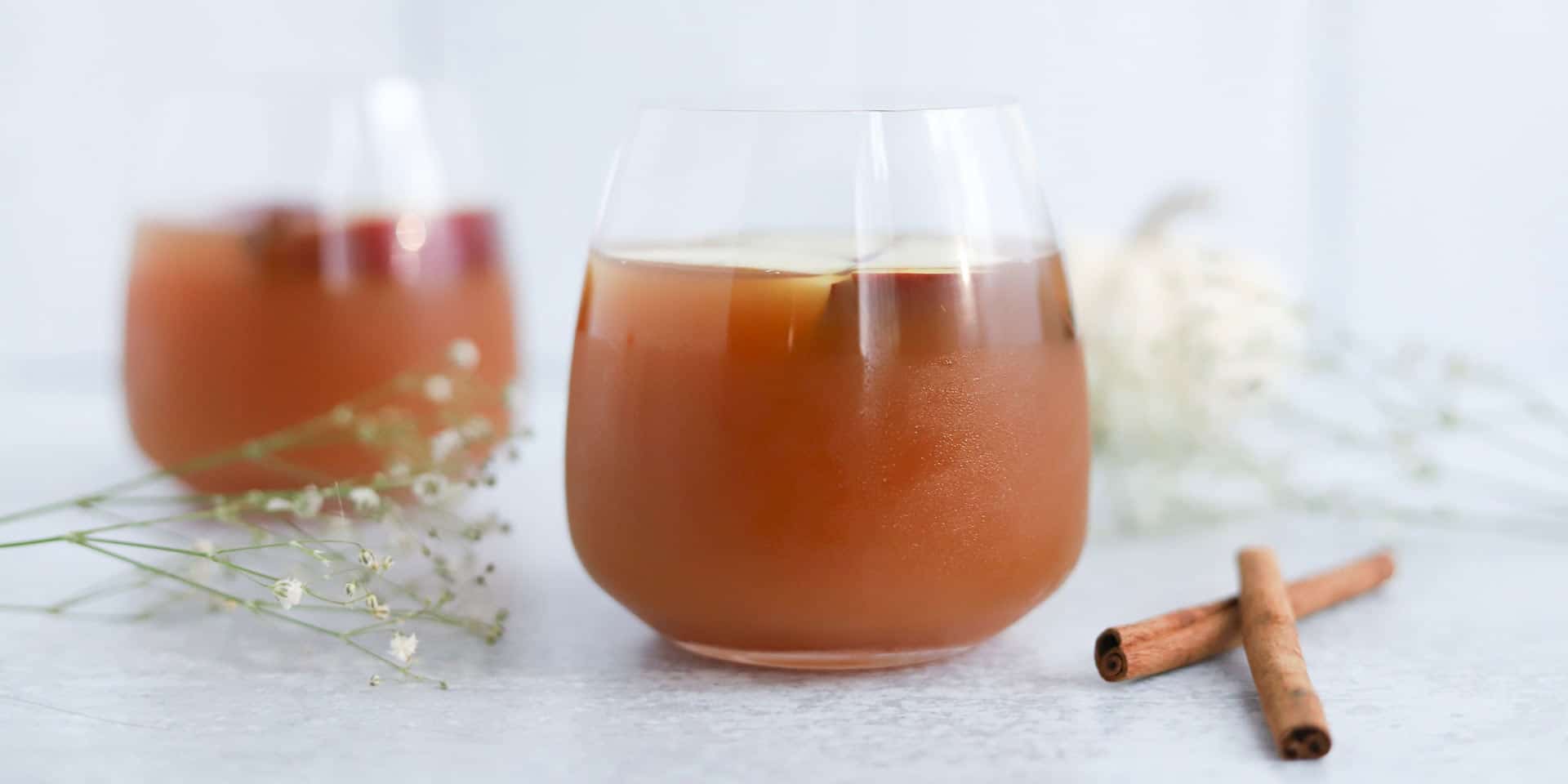 Two glasses of iced tea with a hint of cinnamon, accompanied by delicate white flowers, offering a refreshing moment on a serene backdrop infused with metaphysical energy.