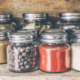 A collection of metaphysical spices and herbs neatly organized in labeled glass jars on a wooden shelf, bringing rustic charm to a spiritual shop's ambiance.