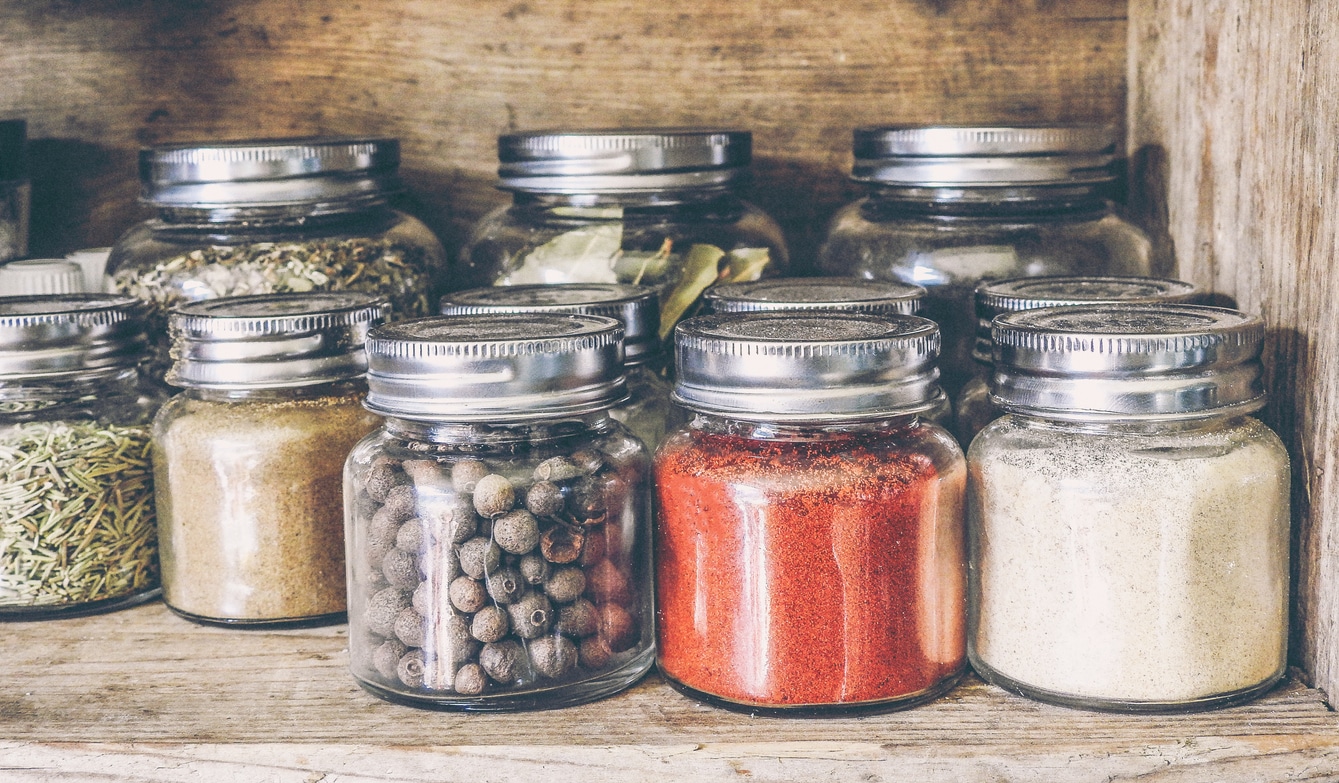 A collection of metaphysical spices and herbs neatly organized in labeled glass jars on a wooden shelf, bringing rustic charm to a spiritual shop's ambiance.