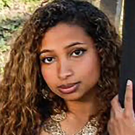A young woman with curly hair and subtle makeup giving a gentle, contemplative gaze in a metaphysical shop.