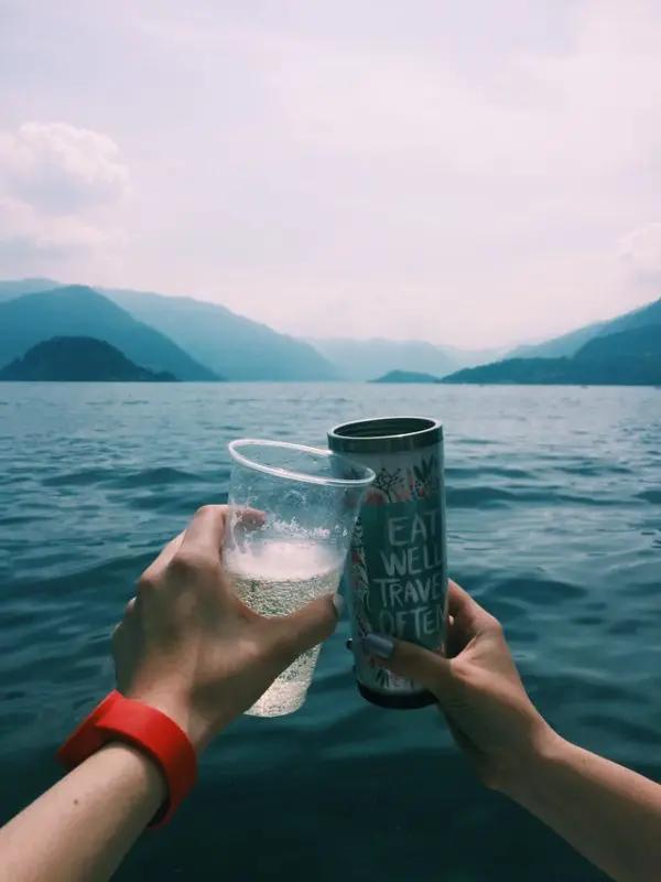 Two people toasting with cups against the backdrop of a serene lake and mountain landscape, embodying the spirit of adventure and friendship, reflective of the new age product vibe.