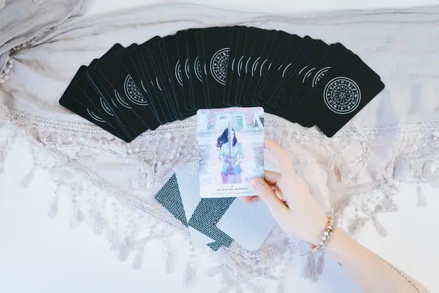 A hand holding a tarot card above a spread of beautifully designed occult tarot cards on a lace cloth.
