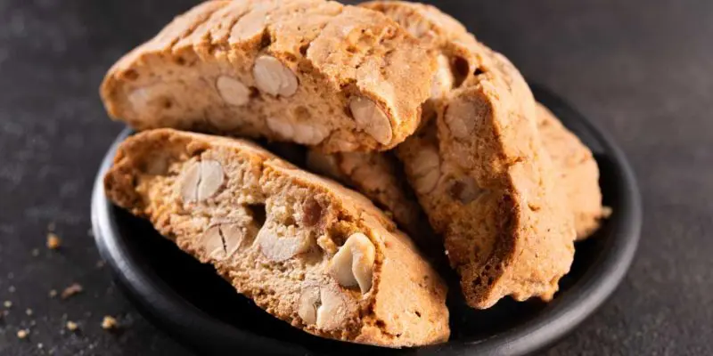 A close-up of almond biscotti arranged on a dark plate, showcasing the crunchy texture and embedded nut pieces, exudes a witchy charm.