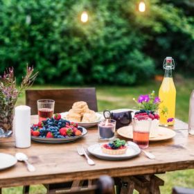 Beltane Foods to Bring to your Fire Festival 21 A summer evening garden party setup with a rustic wooden table adorned with fresh berries, refreshing beverages, floral decorations, and delicate lighting, awaiting guests for a charming outdoor dining experience featuring a corner dedicated to metaph