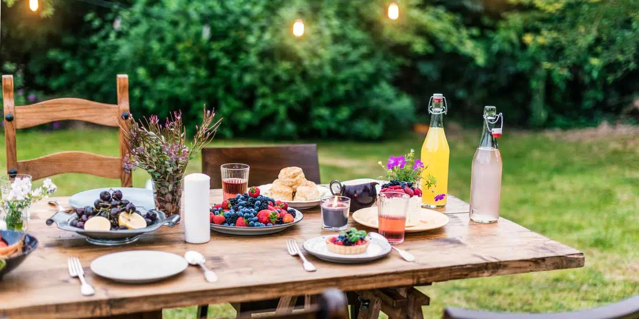 Beltane Foods to Bring to your Fire Festival 1 A summer evening garden party setup with a rustic wooden table adorned with fresh berries, refreshing beverages, floral decorations, and delicate lighting, awaiting guests for a charming outdoor dining experience featuring a corner dedicated to metaph