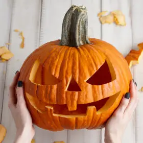 Carving out spooktacular fun: hands proudly presenting a freshly carved jack-o'-lantern with witchy halloween festivities just around the corner.