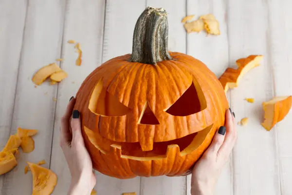 Carving out spooktacular fun: hands proudly presenting a freshly carved jack-o'-lantern with witchy halloween festivities just around the corner.
