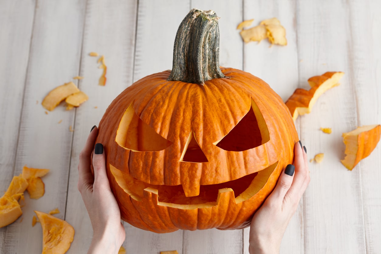 Carving out spooktacular fun: hands proudly presenting a freshly carved jack-o'-lantern with witchy halloween festivities just around the corner.