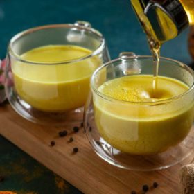 Golden turmeric tea being poured into a clear glass cup, with cookies and spices on a rustic kitchen countertop, creating a warm and healing atmosphere with a spiritual touch.