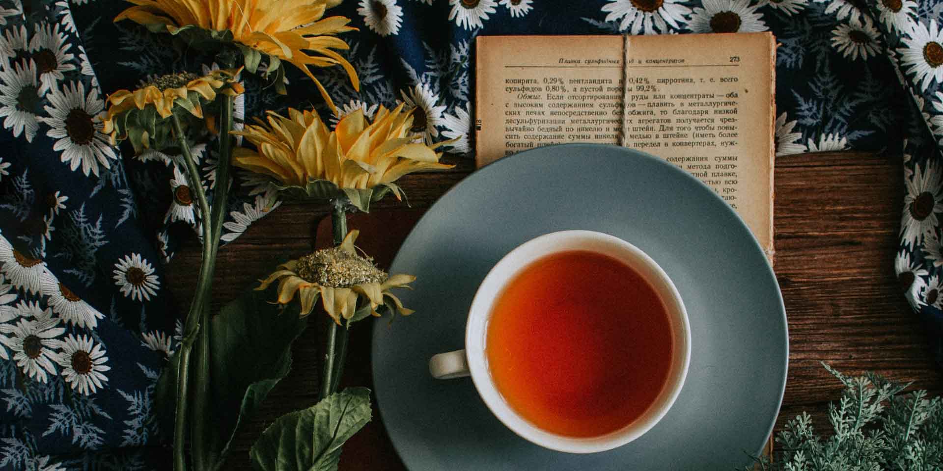 A tranquil tea time: a cup of warm tea nestled amidst a floral backdrop, accompanied by a metaphysical book with sunflowers adding a vibrant touch of nature.