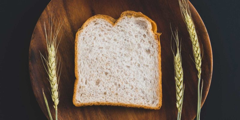Lammas Bread Recipe: White Sandwich Bread for Bread Machine 33 A slice of sandwich bread on a wooden plate with three wheat stalks