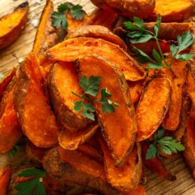 Sweet Potato Oven Wedges for Friendship, Happiness, and Grounding | Kitchen Witchcraft Recipes 8 A wooden cutting board piled with crispy roasted sweet potato wedges garnished with fresh parsley and imbued with new age product energies.
