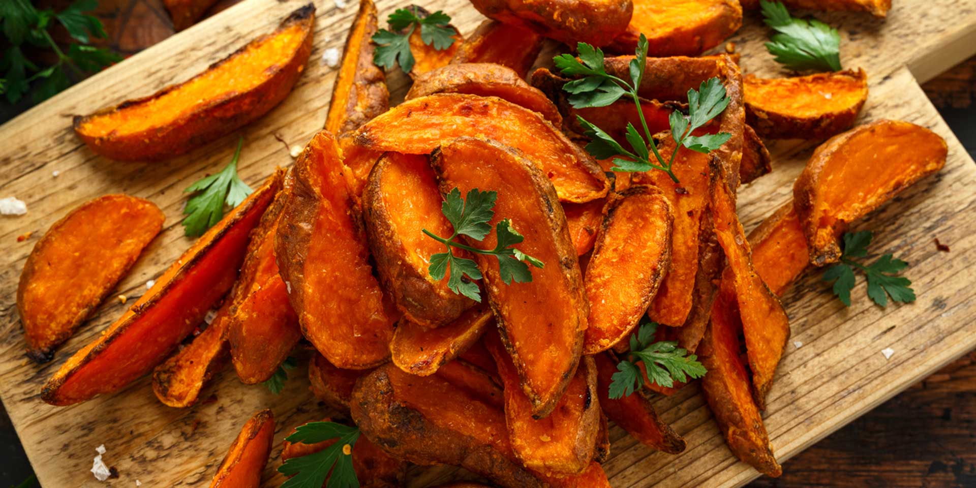 A wooden cutting board piled with crispy roasted sweet potato wedges garnished with fresh parsley and imbued with new age product energies.