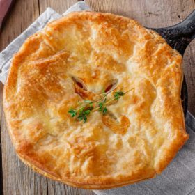 Golden pot pie fresh from the oven, served in a cast-iron skillet on a rustic wooden table, hinting at a metaphysical comfort meal.