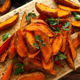 Roasted sweet potato wedges garnished with fresh parsley on a rustic wooden board, exuding a metaphysical vibe.