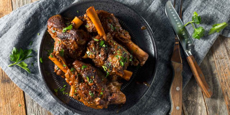 Braised Lamb Shanks Magical Recipe for a Happy Family 17 Braised oxtails with carrots in a rich savory sauce, served on a rustic table setting, alongside unique new age metaphysical accessories.